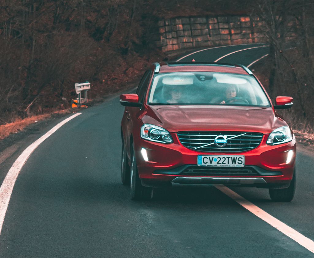 A red Volvo car drives along a curved road in Cătrușa, Romania, showcasing dynamic motion and scenic surroundings.