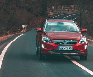 A red Volvo car drives along a curved road in Cătrușa, Romania, showcasing dynamic motion and scenic surroundings.