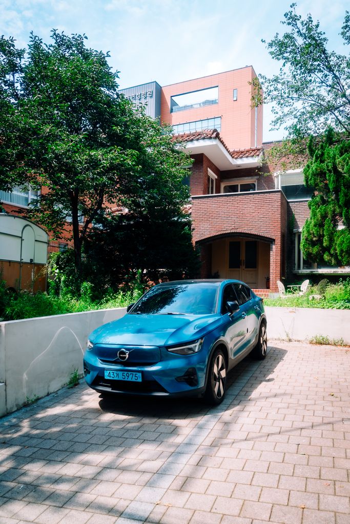 Is the Volvo C40 Electric? A sleek blue electric car parked in a residential driveway in Seoul, South Korea.