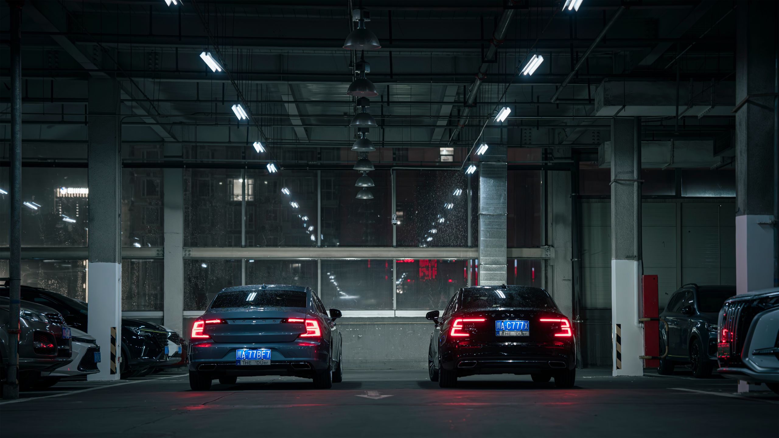 Two modern cars in an urban indoor parking garage during night time, showcasing sleek automotive design.