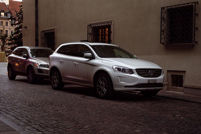 White Volvo SUV parked on cobblestone city street during winter with Christmas decorations.
